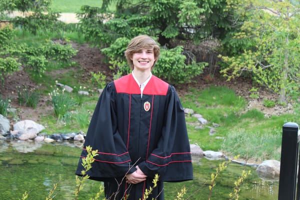 Me in graduation regalia by a pond