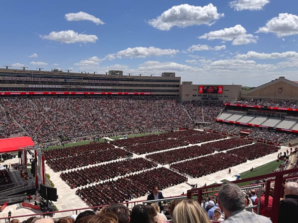 UW-Madison graduation at Camp Randall Stadium with thousands of graduates in red regalia arrayed in columns on the field under a blue sky.