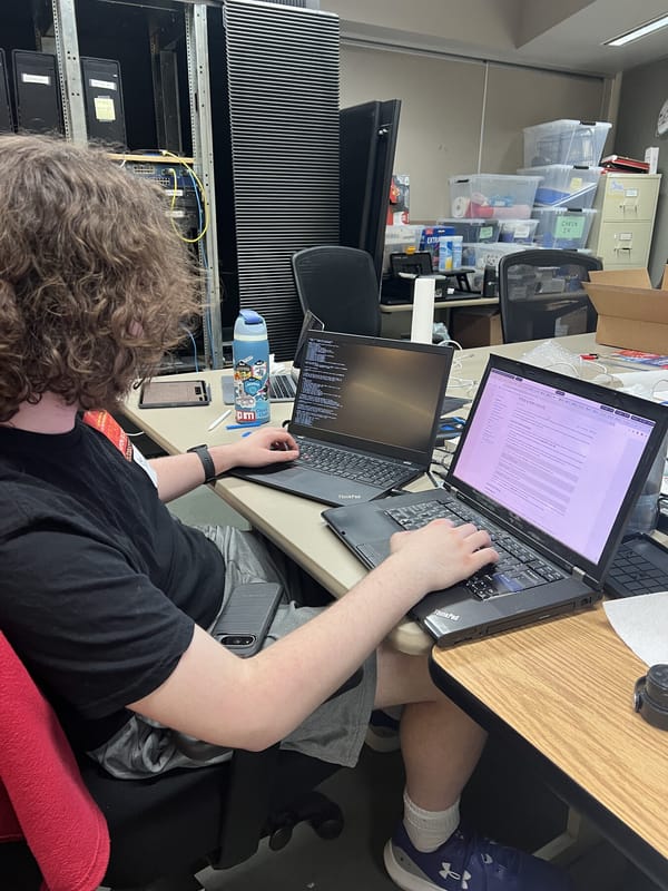 Ben sitting at a desk with two ThinkPads side by side at the table in the UPL, migrating from his old laptop to his newly set-up one.