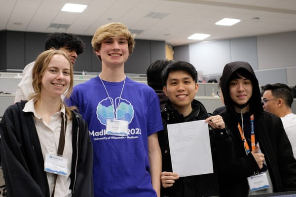 Me in a purple MadHacks 2023 shirt posing with my hackathon team, one teammate holding up our submission paper.