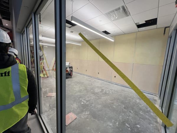 UPL members in a hard hats and safety vests touring the unfinished new UPL space in Morgridge Hall, walking past its glass wall.